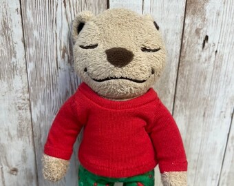 Può includere: Un orso di peluche marrone che indossa una camicia rossa a maniche lunghe e un pigiama a fantasia verde e bianca a tema natalizio.