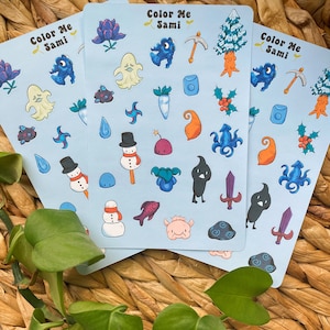 May include: Three sheets of stickers with a blue background and various illustrations. The stickers feature a snowman, a ghost, a fish, a carrot, a tree, a sword, a flower, a pickaxe, a holly berry, and more. The text on the stickers reads "Color Me Sami".