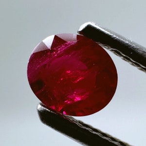 May include: A deep red ruby gemstone with a round cut and a faceted surface.