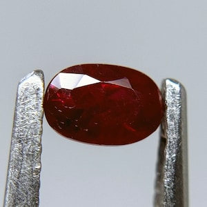 Op de afbeelding: Een dieprode ovale robijn, vastgehouden in een pincet.