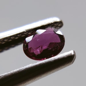 Pode incluir: Um close-up de uma gema oval de cor roxa escura mantida por pinças.