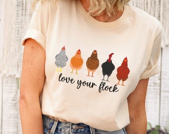 May include: A soft cream t-shirt with a graphic of five chickens in a row, with the text "love your flock" underneath. The model is wearing the shirt with blue jeans.