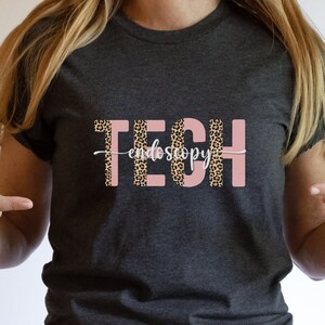 May include: A dark gray t-shirt with a pink and leopard print design that says "TECH endoscopy".