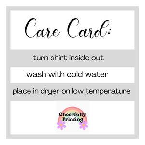 Pode incluir: Cart&atilde;o de cuidados com instru&ccedil;&otilde;es para lavar uma camisa: vire a camisa do avesso, lave com &aacute;gua fria e coloque na secadora em temperatura baixa. O cart&atilde;o tem um gr&aacute;fico de arco-&iacute;ris com o texto "Cheerfully Printing".