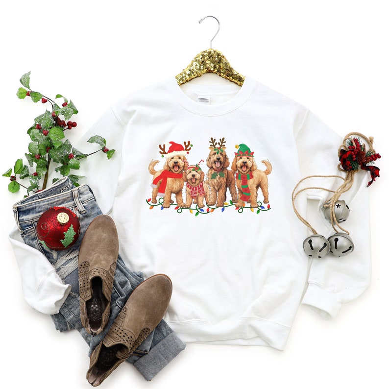 May include: White sweatshirt with a Christmas-themed design featuring four doodle dogs wearing festive hats and antlers. The dogs are standing in front of a string of Christmas lights.