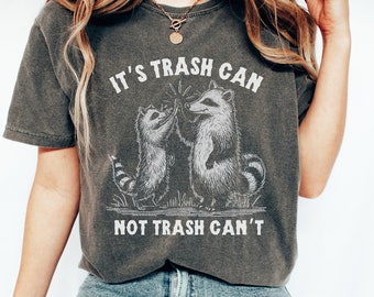 May include: Dark gray t-shirt with the text "IT'S TRASH CAN NOT TRASH CAN'T" and a graphic of two raccoons giving each other a high five. The raccoons are in black and white, and the text is in white.