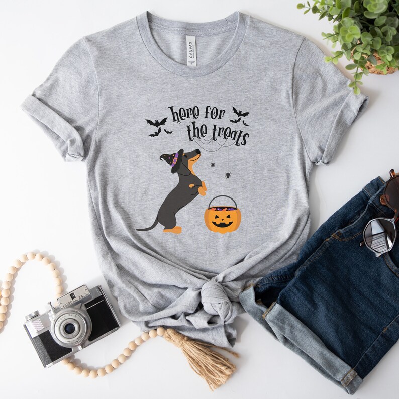 K&ouml;nnte beinhalten: Graues T-Shirt mit einem schwarzen und braunen Dackel, der einen Hexenhut tr&auml;gt und einen K&uuml;rbis-Eimer h&auml;lt. Der Text "here for the treats" ist auf dem Shirt aufgedruckt.