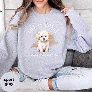 K&ouml;nnte beinhalten: Ein graues Sweatshirt mit dem Text "Life is Great" und einer Aquarell-Illustration eines wei&szlig;en Cavapoo-Welpen. Der Text "cavapoos make it better" befindet sich unter dem Welpen.