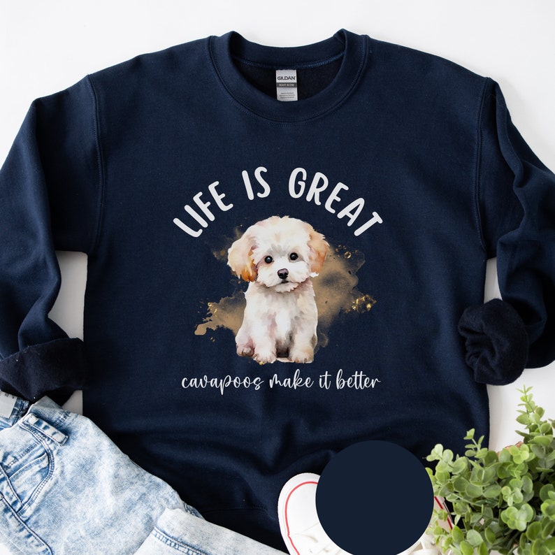 K&ouml;nnte beinhalten: Ein marineblauer Pullover mit einer wei&szlig;en Aquarell-Illustration eines Cavapoo-Welpen. Der Text "Life is great cavapoos make it better" ist auf dem Pullover aufgedruckt.