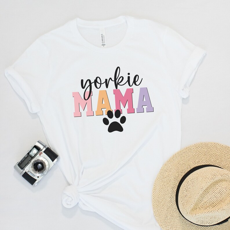 May include: White t-shirt with the text "yorkshire mama" in colorful letters and a black paw print.