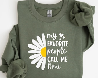 May include: Olive green sweatshirt with a daisy graphic and the text "my FAVORITE people CALL ME Omi". The daisy has white petals and a yellow center. The sweatshirt has long sleeves and a crew neck.