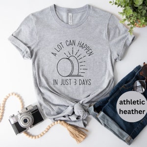 Pode incluir: Uma camiseta cinza com o texto "A lot can happen in just 3 days" e um gr&aacute;fico de um nascer do sol sobre uma pedra. O texto est&aacute; em preto e o gr&aacute;fico est&aacute; em preto e branco.