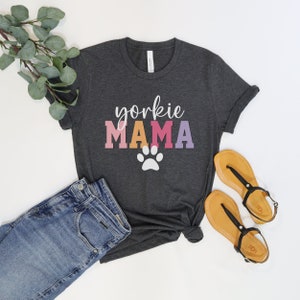 May include: A dark gray t-shirt with the text "yorkshire mama" in colorful letters and a white paw print.