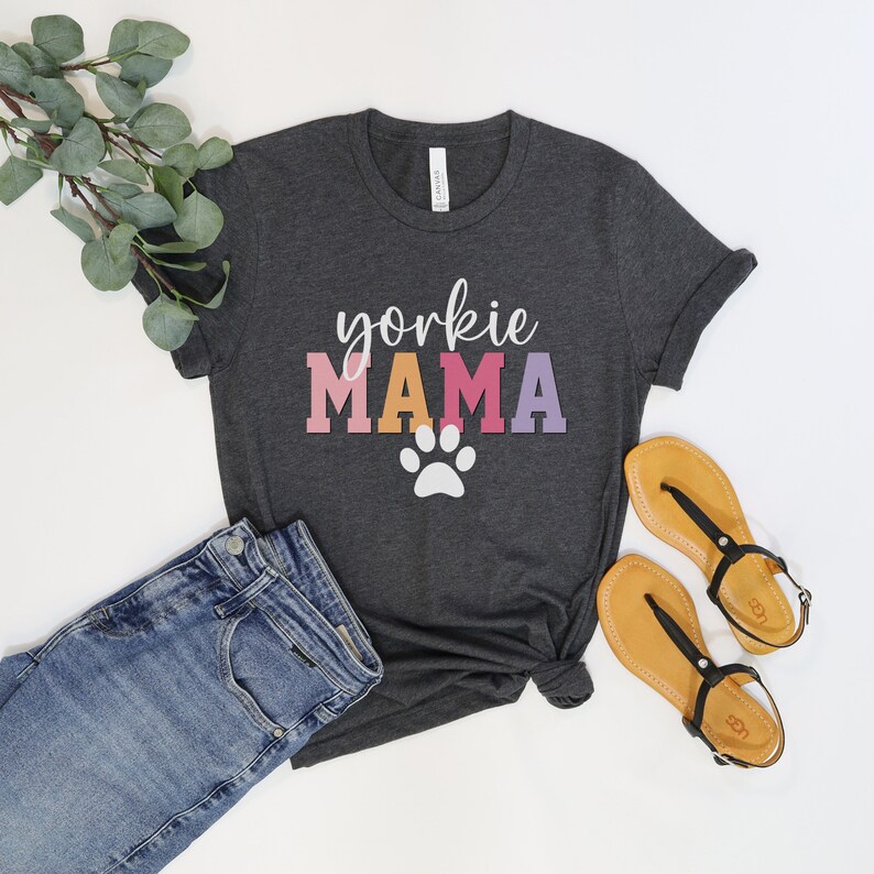 May include: A dark gray t-shirt with the text "yorkshire mama" in colorful letters and a white paw print.