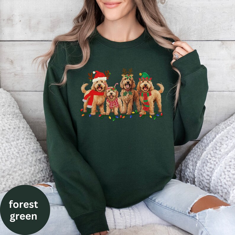 May include: A forest green sweatshirt with a Christmas-themed design featuring four doodle dogs wearing festive hats and antlers. The dogs are standing in front of a string of Christmas lights.