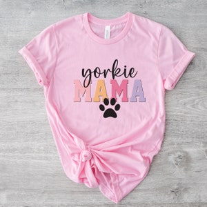 May include: Pink t-shirt with the text "yorkie MAMA" in rainbow colors and a black paw print.