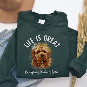 May include: A dark green sweatshirt with a watercolor illustration of a cavapoo dog. The text "Life is Great Cavapoos make it better" is printed in white on the sweatshirt.