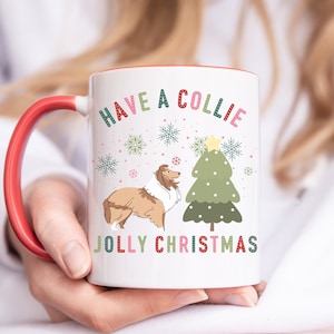 May include: White ceramic mug with a red rim. The mug features a cartoon Collie dog standing next to a green Christmas tree with a yellow star on top. The text "Have a Collie Jolly Christmas" is printed on the mug.