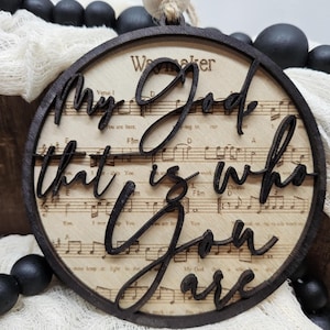 May include: A round wooden ornament with the words "My God that is who you are" cut out in the wood. The ornament is decorated with a musical note background.