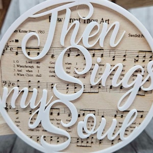Puede incluir: Adorno blanco recortado con las palabras "Then Sings My Soul" sobre un fondo de partituras antiguas. La música incluye las palabras "How Great Thou Art" y "Swedish Psalm".