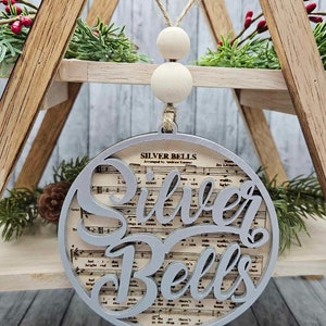 May include: A silver ornament with the words "Silver Bells" cut out of the design. The ornament is decorated with a sheet music background.