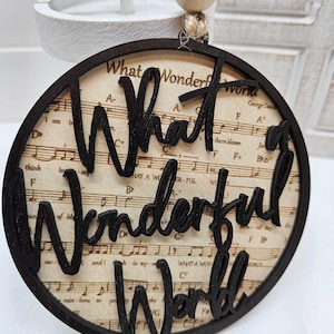 以下が含まれることがあります： 「What a Wonderful World」という文字が切り抜かれた黒い木製オーナメントで、楽譜の背景があります。