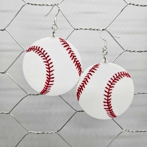 May include: A pair of white baseball earrings with red stitching. The earrings are hanging from silver hooks.