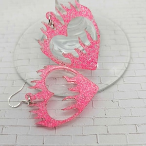 Puede incluir: Pendientes de corazón rosa con purpurina y diseño de llama.
