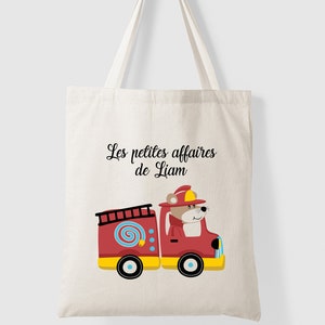 Peut inclure: Un sac fourre-tout en toile blanche avec du texte noir qui dit "Les petites affaires de Liam". Une illustration de dessin animé d'un camion de pompiers rouge avec un ours portant un casque de pompier conduisant le camion est sur le sac.