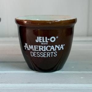 May include: A brown ceramic bowl with a white rim and the text "JELL-O Brand AMERICANA DESSERTS" printed on the side.