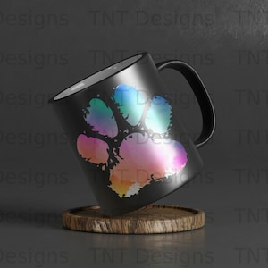 May include: A black ceramic mug with a colourful paw print design. The mug has a white interior and a handle. The mug is sitting on a wooden coaster.
