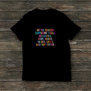 K&ouml;nnte beinhalten: Schwarzes T-Shirt mit einer regenbogenfarbenen Botschaft, die lautet: "Sei der Grund, warum sich jemand willkommen, gesehen, geh&ouml;rt, gesch&auml;tzt, geliebt und unterst&uuml;tzt f&uuml;hlt."