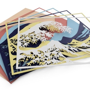 May include: A layered paper art piece depicting the Great Wave off Kanagawa, a famous Japanese woodblock print by Hokusai. The wave is cut out in white paper and layered on top of blue, yellow, pink, and beige paper.