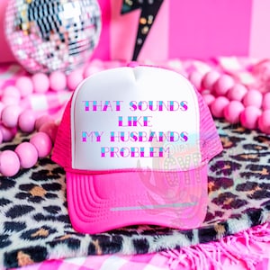 May include: A pink and white trucker hat with the text "That sounds like my husbands problem" in blue and pink lettering.