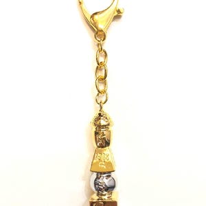 May include: Gold-tone keychain with a small, multi-tiered pagoda charm. The charm features a silver-tone sphere and intricate details.