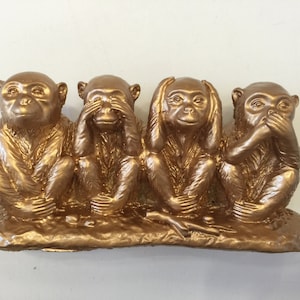 May include: Four gold-painted monkey figurines, each with a different gesture: one covering its eyes, one covering its ears, one covering its mouth, and one with its hands open. The monkeys are sitting on a gold-painted base.