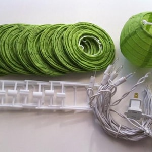 Puede incluir: Un conjunto de faroles de papel verde, una estructura de farol de plástico blanco y una cadena de luces. Los faroles son redondos y plegados, con un farol montado. Las luces tienen un enchufe estándar.