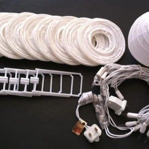 Puede incluir: Un conjunto de faroles de papel blancos y luces de cadena, ideal para iluminación decorativa. La imagen muestra varios marcos de farolillos circulares planos, un farolillo redondo completamente montado, un marco de plástico y una cadena de luces.