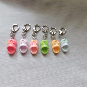 May include: Six colorful miniature sandal keychains. Each sandal is a different color: pink, lavender, peach, green, orange, and light blue. The sandals have silver-colored metal clasps.