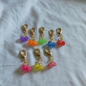 May include: Seven colorful dice charms with gold lobster clasps. The dice are in the colors purple, orange, green, blue, red, yellow, and pink.