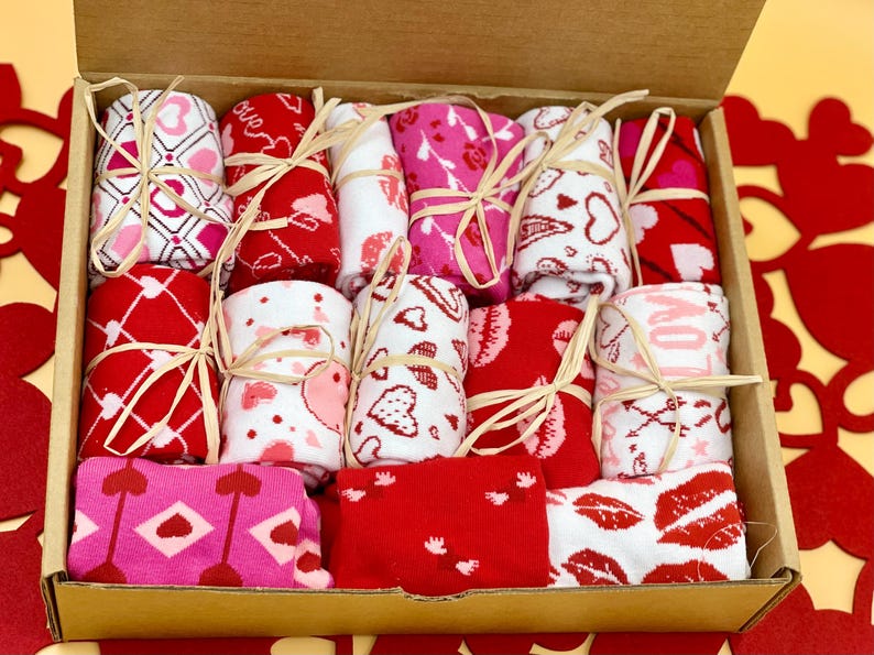 May include: A box filled with pairs of colorful socks with heart and love themed patterns. The socks are tied with twine and arranged in a neat pattern.