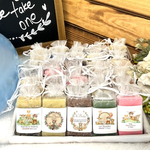 May include: A collection of small, wrapped bars of soap with woodland animal designs and personalized messages. The soaps are arranged in a white basket with a sign that reads "Please take one".