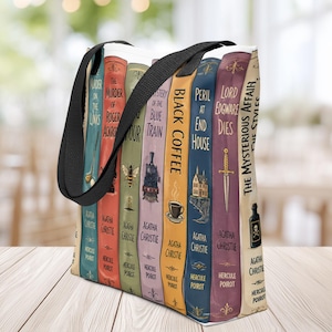 Op de afbeelding: Een draagtas met een print van diverse Agatha Christie boekruggen, waaronder Murder on the Links, The Murder of Roger Ackroyd, Black Coffee, Peril at End House, Lord Edgware Dies en The Mysterious Affair at Styles, voorzien van zwarte hengsels.