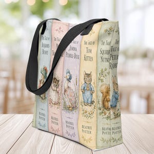Peut inclure: Un sac fourre-tout avec des anses en tissu noir présentant une impression verticale de dos de livres d'histoires de Beatrix Potter, incluant The Tale of Benjamin Bunny, The Tale of Jemima Puddle-Duck, The Tale of Tom Kitten, The Tale of Squirrel Nutkin et The Tale of Peter Rabbit.