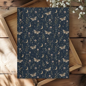 May include: A dark blue fabric with a repeating pattern of butterflies, crescent moons, small flowers, and stars. The butterflies are tan and white, and the moons and stars are gold. The flowers are a light pink color. The fabric is displayed on a wooden tray.
