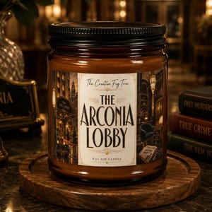 Puede incluir: Una vela en frasco de vidrio marrón con tapa negra, con una etiqueta que dice The Creative Fig Tree The Arconia Lobby 255g vela de soja, con una ilustración de un vestíbulo, sobre una base circular de madera.
