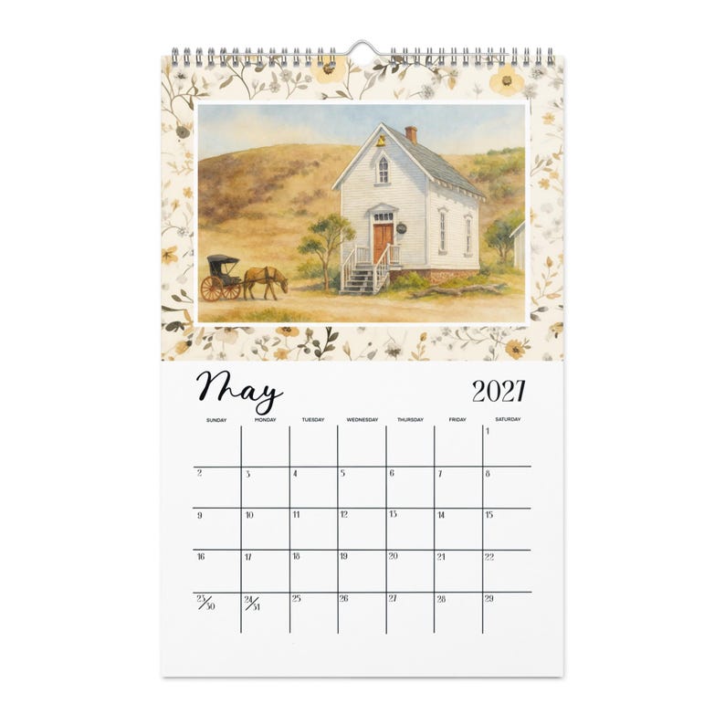 May include: A wall calendar for May 2021 featuring a watercolor illustration of a white schoolhouse with a brown door and a horse-drawn carriage on a dirt path. The border is decorated with a floral pattern in muted yellow, brown, and green tones.