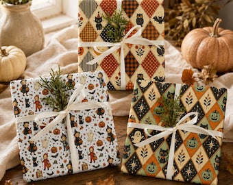 May include: Three square gifts wrapped in patterned paper featuring Halloween motifs like black cats, pumpkins, ghosts, and owls. Each package is tied with a white ribbon and decorated with a small sprig of green foliage on the top centre.