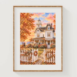 Könnte beinhalten: Ein gerahmter Kunstdruck zeigt ein weißes viktorianisches Haus mit Veranda, umgeben von herbstlichem Laub in Orange- und Gelbtönen. Ein weißer Lattenzaun mit einem Kranz führt zum Haus unter einem Sonnenuntergangshimmel nahe dem Meer.