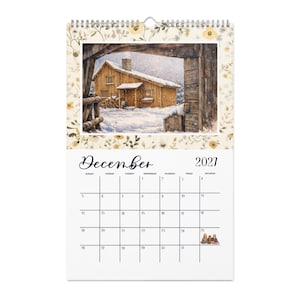 May include: A wall calendar for December 2021 featuring a spiral binding at the top. The upper section displays a watercolor illustration of a wooden cabin in a snowy landscape. The lower section shows a grid with the month name and dates.